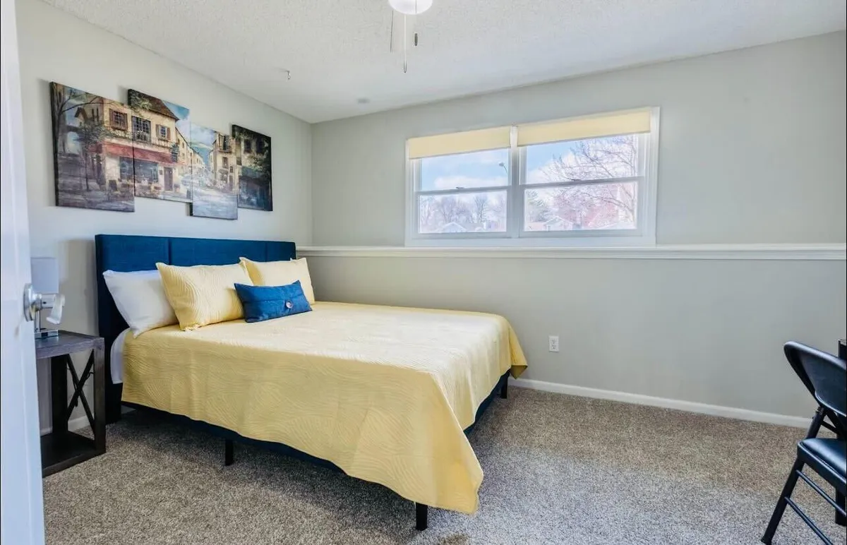 A serene bedroom scene featuring a plush bed dressed in vibrant yellow bedding, illuminated by gentle natural light streaming through a window. Tasteful artwork on the wall and soft, cozy textures create a peaceful ambiance ideal for relaxation and restful sleep.