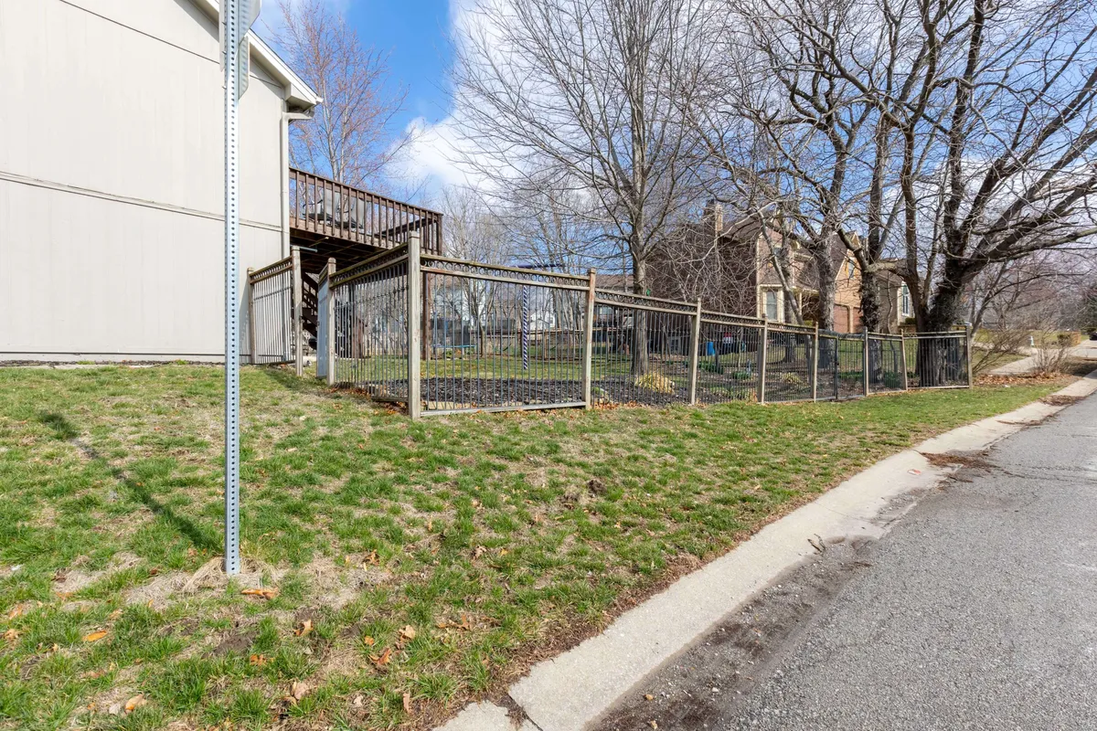 This exterior image showcases a welcoming backyard surrounded by mature trees, featuring a fenced area and an inviting deck. Families and children are seen enjoying the space, with vibrant seasonal touches such as spring blooms and autumn leaves adding visual interest. The deck is set up for gatherings, hinting at sociable summer evenings outdoors.